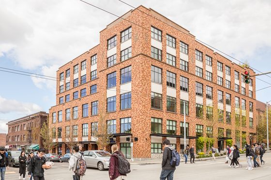 Street view of Russell Hall, a modern six-story brick apartment building with large windows on a busy corner, surrounded by pedestrians and parked cars in an urban neighborhood.