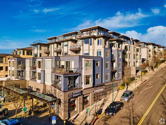 Exterior view of Westwater Apartments, a modern mid-rise building with retail on the ground floor, including a Jimmy John’s, located on a sloped street with balconies and large windows throughout.