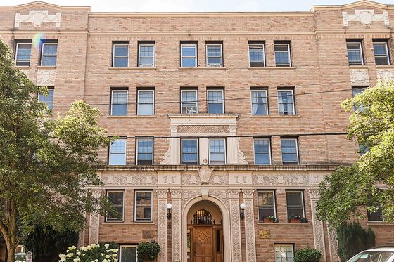 Front view of The Whitworth, a historic brick apartment building with decorative stone detailing around the entryway and windows, framed by trees on a sunny day.