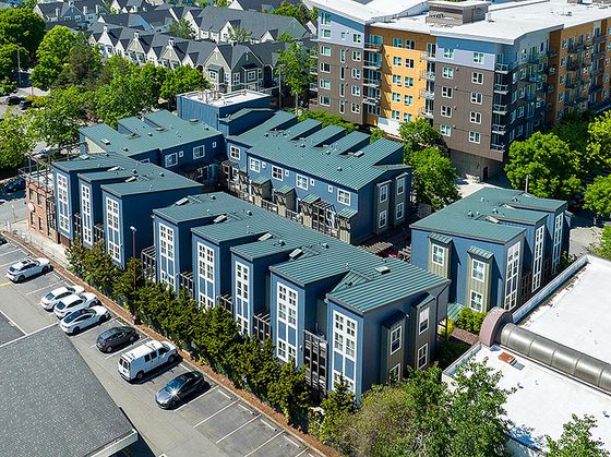 Aerial view of the Urbane apartment community, showcasing modern townhome-style units with green roofs alongside mid-rise buildings, surrounded by trees and suburban development in a lush, green neighborhood.