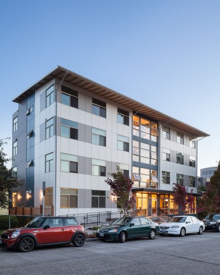 Front entrance of The Yobi Apartments, featuring blue and white siding, large windows, and black railings along a stairway leading to the main door.
