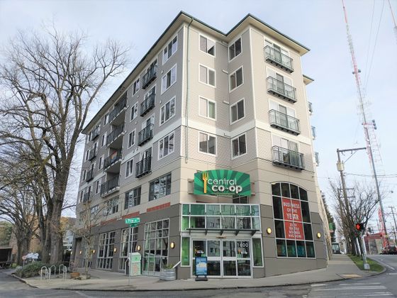 Exterior view of a multi-story apartment building with retail space on the ground floor, including a Central Co-op grocery store at the corner of East Pine Street and 16th Avenue in Seattle.