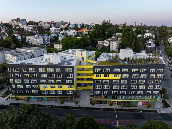 Aerial view of Hilite Apartments, a modern dark-gray building with bright yellow accents and rooftop greenery in a residential Seattle neighborhood.