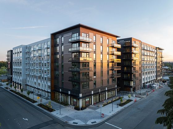 Exterior view of Ember Apartments, a modern multi-story building with wood and dark paneling, large windows, and balconies reflecting the sunset.