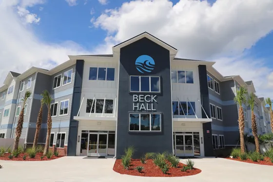 Modern Beck Hall apartment complex with stylish architecture and vibrant landscaping under a clear blue sky.