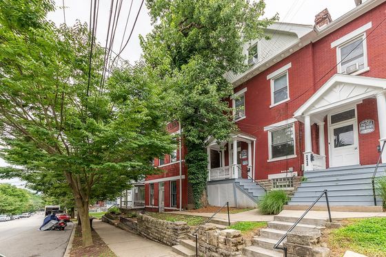 Charming brick townhouse with a welcoming porch, surrounded by lush greenery on a quiet street.