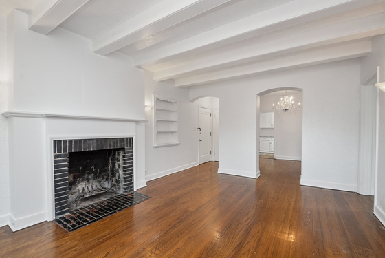 Elegant living room with hardwood floors, a classic fireplace, and bright, spacious ambiance connecting to a modern kitchen with chandelier lighting.