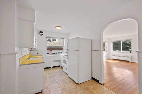 Bright retro kitchen with yellow countertops and white cabinets, leading into a sunlit living area with hardwood floors and large windows.