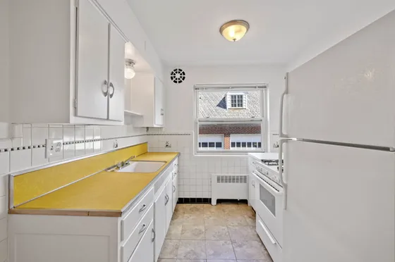 Bright and charming kitchen with retro yellow countertops, ample white cabinetry, and a large window letting in natural light.
