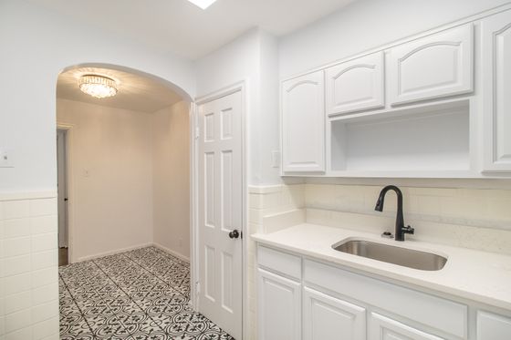 Bright kitchen with elegant white cabinetry, sleek black faucet, and charming patterned tile flooring under a sparkling chandelier.