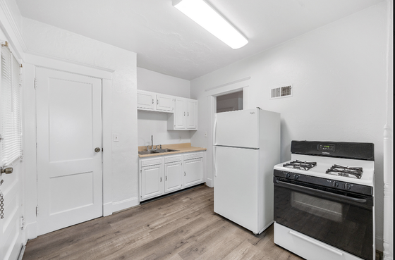 Bright and modern kitchen featuring sleek white cabinetry, a spacious refrigerator, and a classic gas stove, with elegant wood flooring.