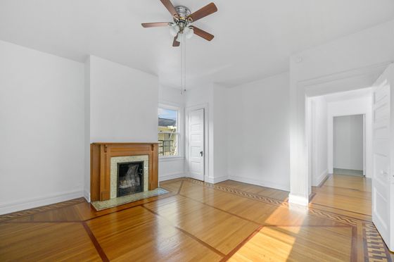 Bright and airy room with elegant hardwood floors, a charming fireplace, and ceiling fan, perfect for cozy living.