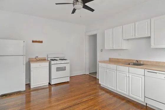 Bright and spacious kitchen with modern white cabinetry, sleek wooden floors, and a ceiling fan.