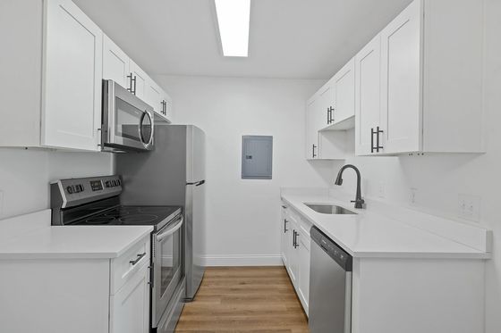Modern kitchen with sleek stainless steel appliances, white cabinetry, and elegant wood flooring, offering a clean and stylish culinary space.