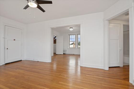 Bright and airy living space with polished hardwood floors, elegant ceiling fan, and large windows offering natural light.