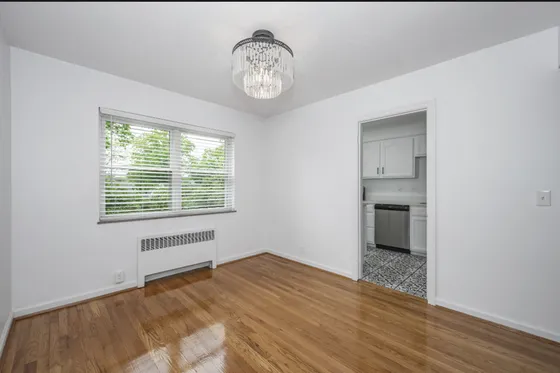 Bright and inviting apartment room with hardwood floors, modern chandelier, and view into a stylish kitchen with patterned tiles.