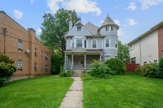 Charming Victorian-style home with a turret and inviting front porch, surrounded by lush greenery and vibrant landscaping.
