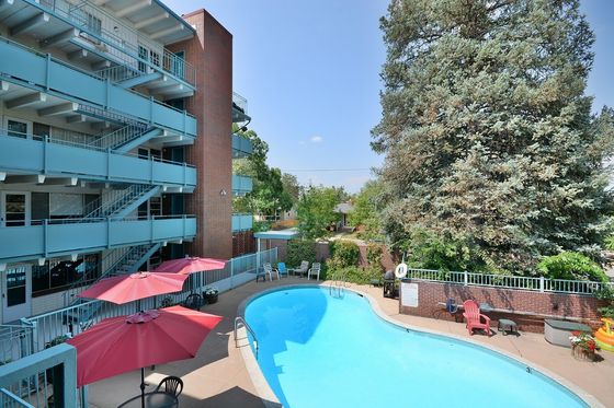 Inviting apartment complex with a scenic outdoor swimming pool, red umbrellas, and lush greenery.