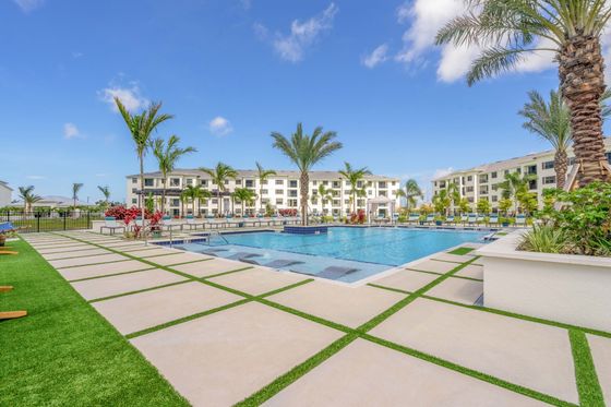 Luxurious apartment complex with a stunning poolside area, surrounded by lush palm trees and modern architecture under a clear blue sky.