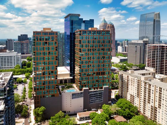 Luxurious urban high-rise with glass facades featuring stunning city views, surrounded by vibrant skyscrapers and lush greenery.