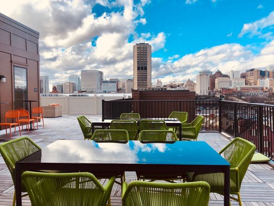 Stylish rooftop terrace with green seating offering stunning cityscape views under a vibrant blue sky.