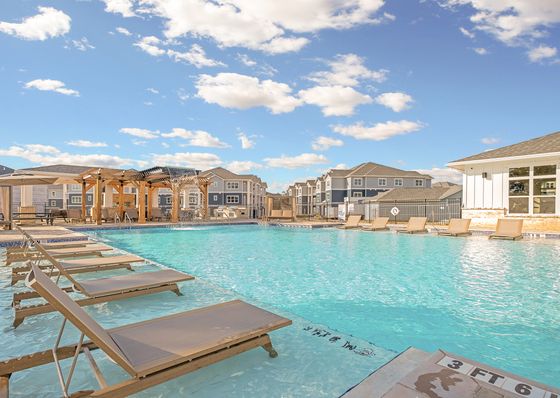 Luxurious outdoor pool area with stylish loungers and a stunning water feature under a clear blue sky.