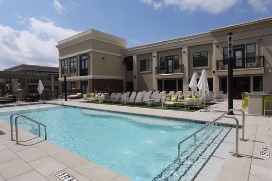 Luxurious apartment complex with a sparkling outdoor pool, surrounded by modern lounge chairs and inviting sun umbrellas, ideal for relaxation.