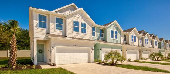 Charming townhouse with modern design, featuring a two-car garage, lush greenery, and a welcoming front entrance.