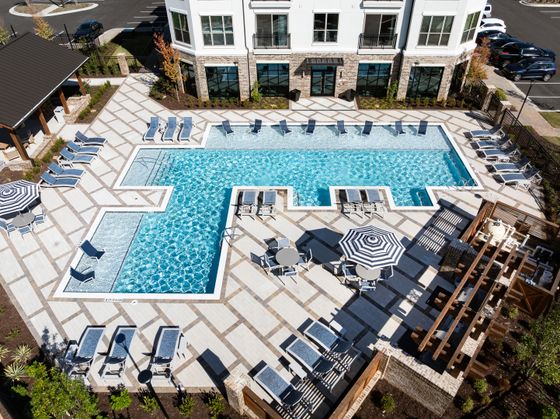 Luxurious apartment complex featuring a stunning outdoor pool with modern lounge chairs and stylish sun umbrellas, perfect for relaxation and entertainment.