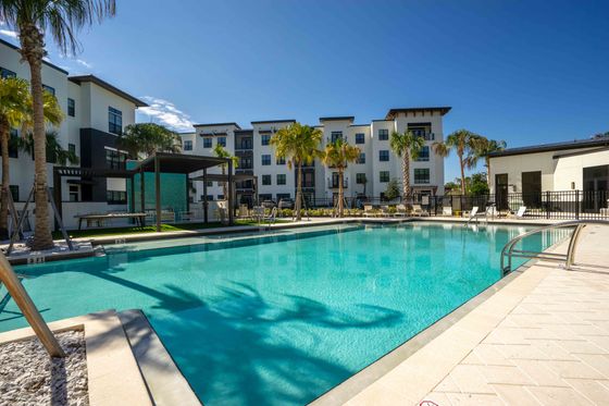 Luxurious apartment complex with a sparkling pool, surrounded by lush palm trees and modern architecture, perfect for resort-style living.