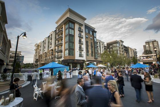 Vibrant urban living captured in a bustling street event outside a modern, multi-story apartment complex with elegant architectural design and lively community gathering.