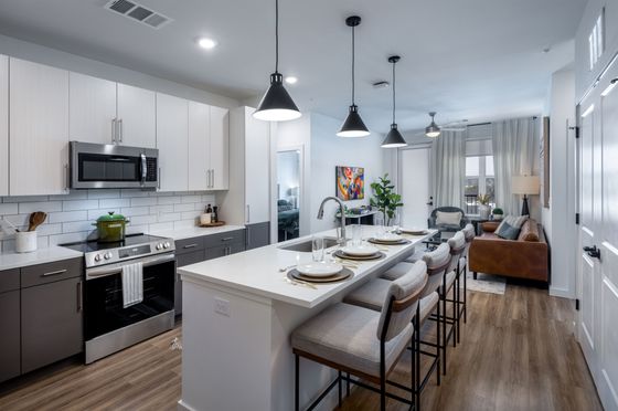 Modern open-concept kitchen and living area with sleek white countertops, stylish bar stools, and cozy seating in a bright, inviting apartment.