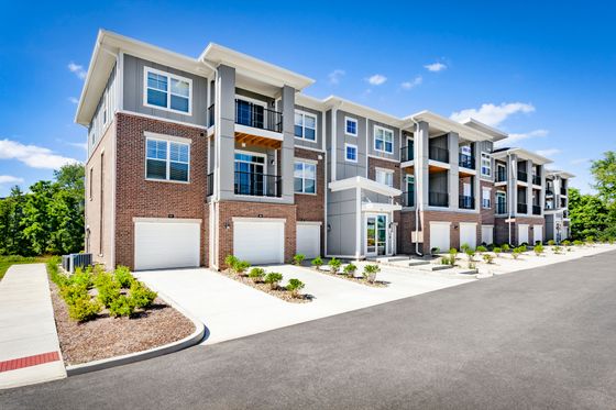 Modern apartment complex with elegant brick facade, featuring multiple levels, individual balconies, and attached garages surrounded by well-maintained landscaping under a clear blue sky.