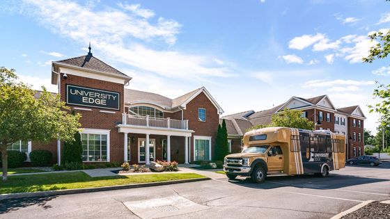 Charming red-brick apartment building with elegant white trim at University Edge, featuring a welcoming entrance and convenient shuttle service under a bright blue sky.