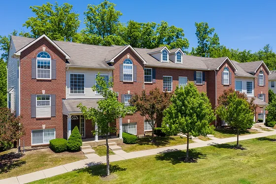 Charming brick townhouse with large windows set against a lush green backdrop, featuring manicured lawns and a peaceful neighborhood ambiance.