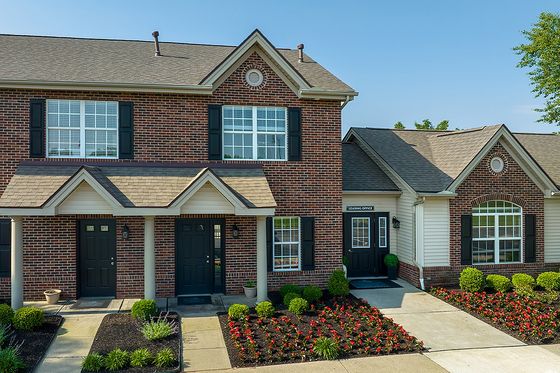 Charming brick apartment building with black shutters, landscaped flower beds, and inviting entrances.