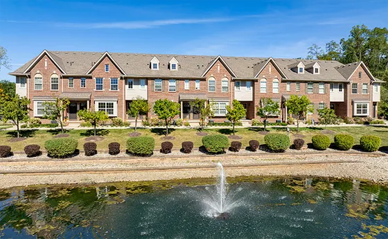 Elegant townhouse complex with classic architecture, lush landscaping, and a serene pond with fountain, offering tranquil living.
