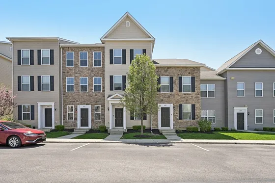 Charming townhouse exterior with stone and siding accents, surrounded by lush greenery and a clear blue sky.