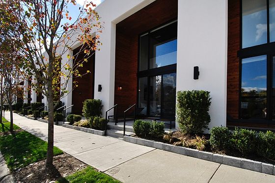 Modern apartment complex exterior with large windows, pristine landscaping, and stylish architecture under a bright blue sky.
