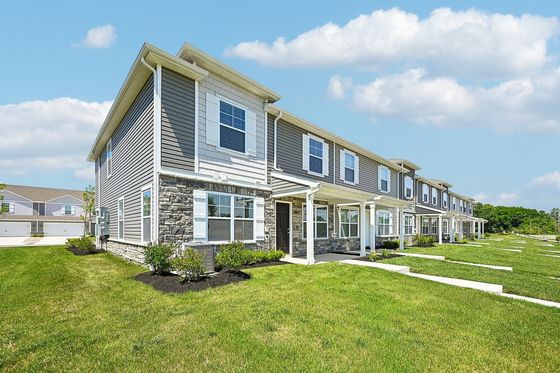 Charming modern townhouse complex with stone accents, manicured lawns, and inviting porches under a bright blue sky.