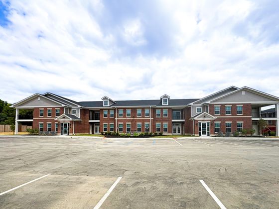 Modern brick apartment complex with stylish gabled roof, ample parking, and lush surroundings under a vibrant sky.