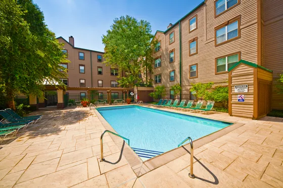 Inviting apartment community with a sunlit outdoor pool, surrounded by lush greenery and comfortable lounge chairs.