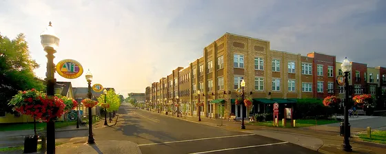 Charming street view of modern apartment community with vibrant brick facades and lush hanging flower baskets, illuminated by warm streetlights.
