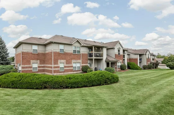 Charming apartment community with brick facade, lush greenery, and a well-maintained lawn.