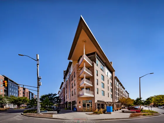 Stunning modern apartment building with unique geometric architecture and stylish balconies, set against a clear blue sky in a vibrant urban neighborhood.