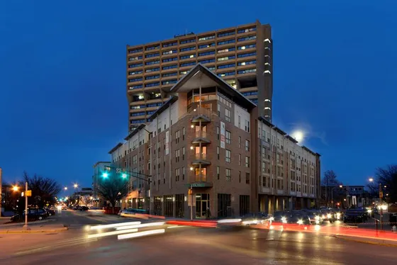 Stunning evening view of a modern high-rise apartment building in a vibrant urban setting, showcasing sleek architecture and bustling city life.
