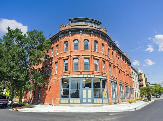 Charming historic red-brick building with large arched windows and intricate architectural details, ideally set on a sunlit corner under a vibrant blue sky.