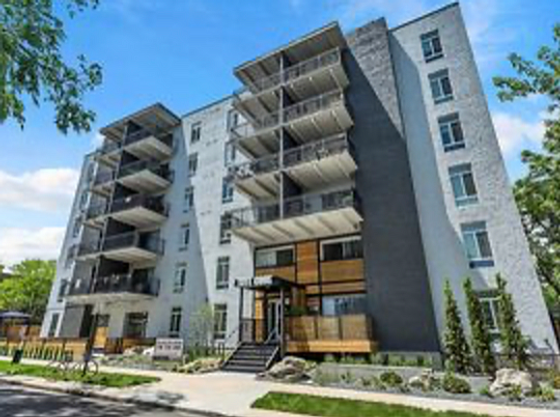 Modern apartment building with sleek balconies and a stylish entrance, set in a lush, green neighborhood.