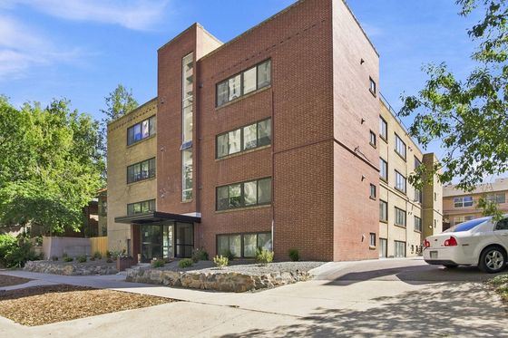Charming brick apartment building with modern architecture, surrounded by lush greenery and a bright blue sky.
