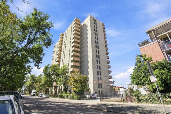 Modern high-rise apartment building with spacious balconies set against a clear blue sky, surrounded by lush greenery on a peaceful street.